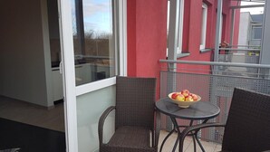 Ein Balkon mit Korbstühlen, einem Tisch mit Obstschale und einem roten Gebäude im Hintergrund.