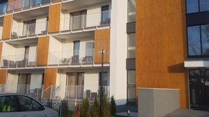 A modern multi-story residential building with balconies, a parking area, and a small garden.
