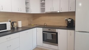 A modern kitchen with white cabinets, a microwave, a kettle, a coffee maker, and an oven.