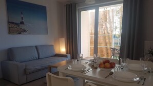 A dining area with a table set for four, a grey sofa, and a painting of a lighthouse on the wall.
