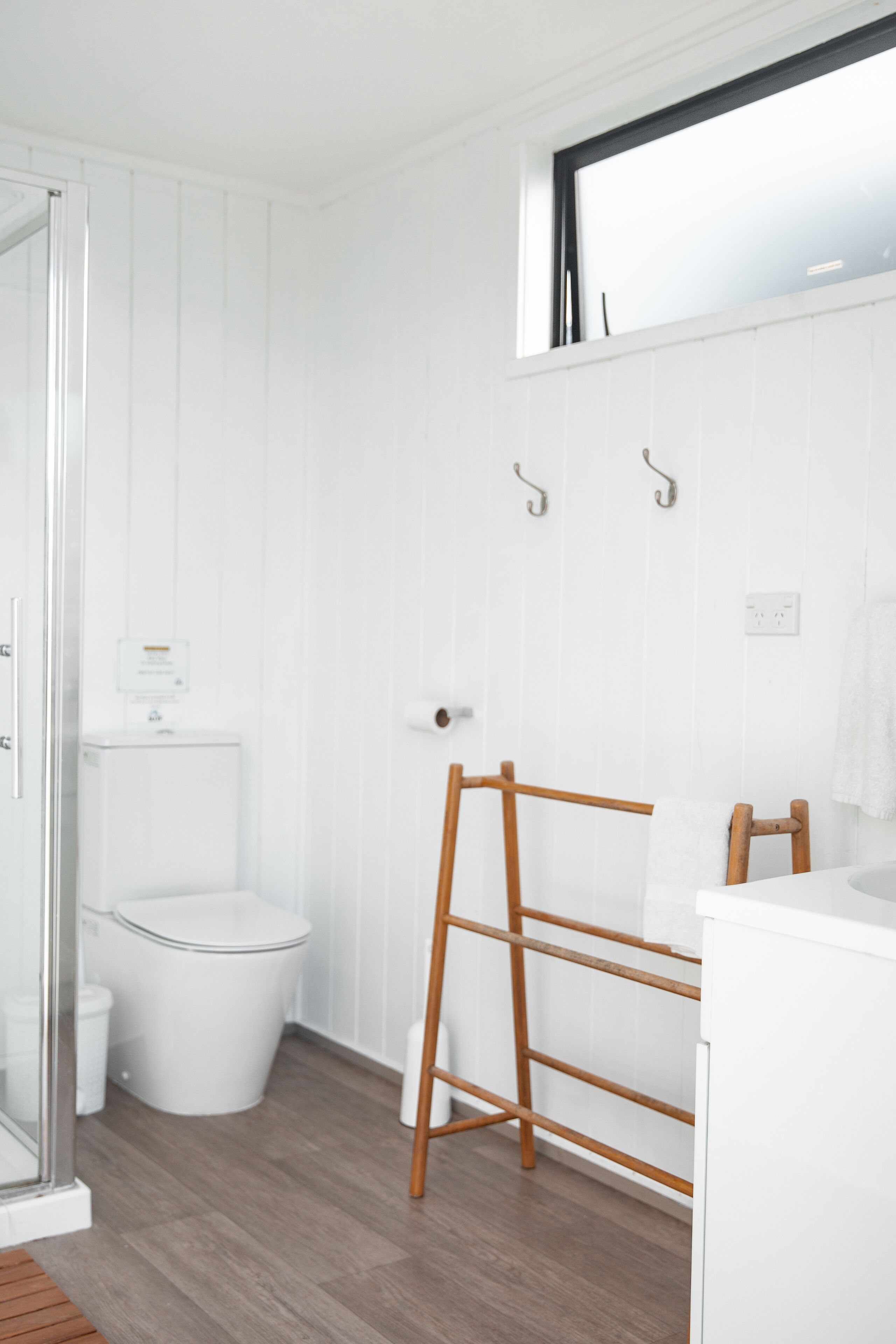 A bathroom with a toilet, a shower, and a wooden rack.