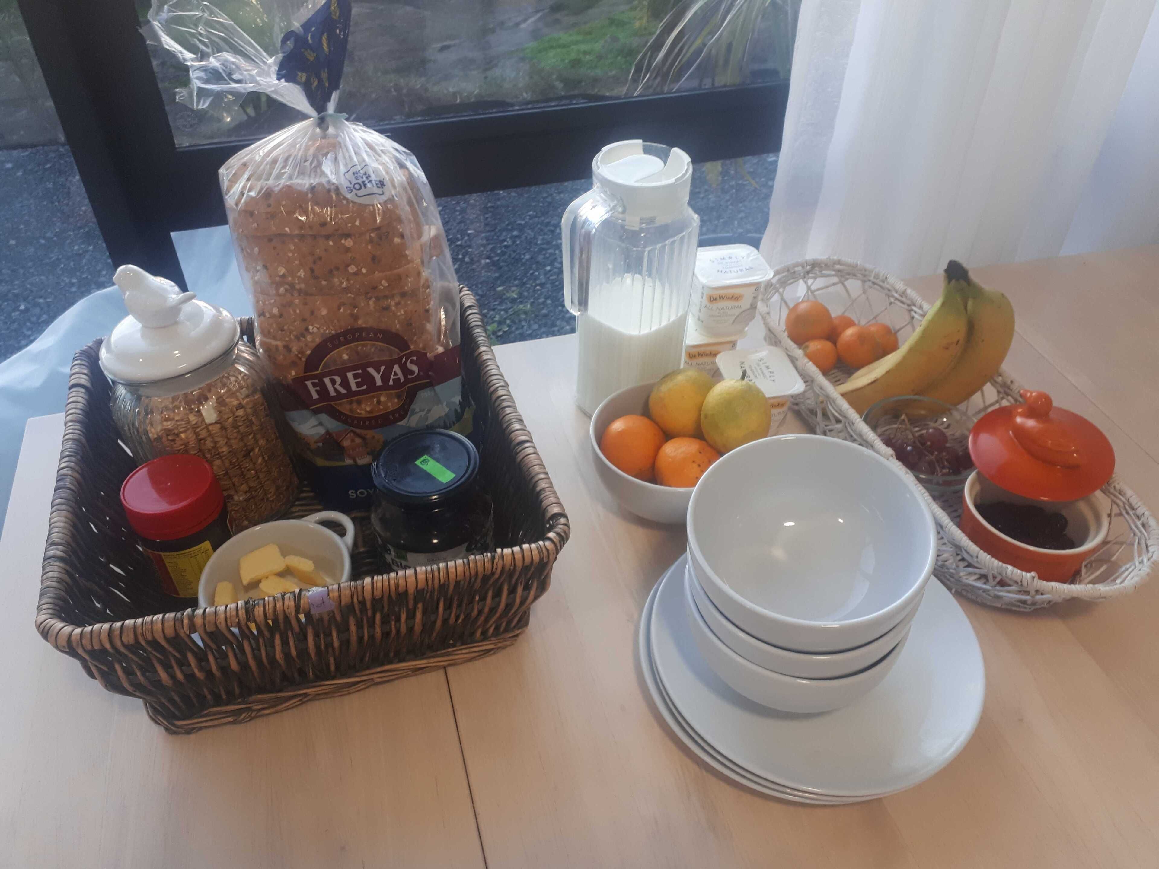 A breakfast tray with bread, butter, jam, milk, and fruits.