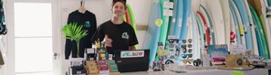 A surf shop with various surfboards, sunglasses, and a laptop. - Aotearoa Surf Eco Pods (Te Arai)