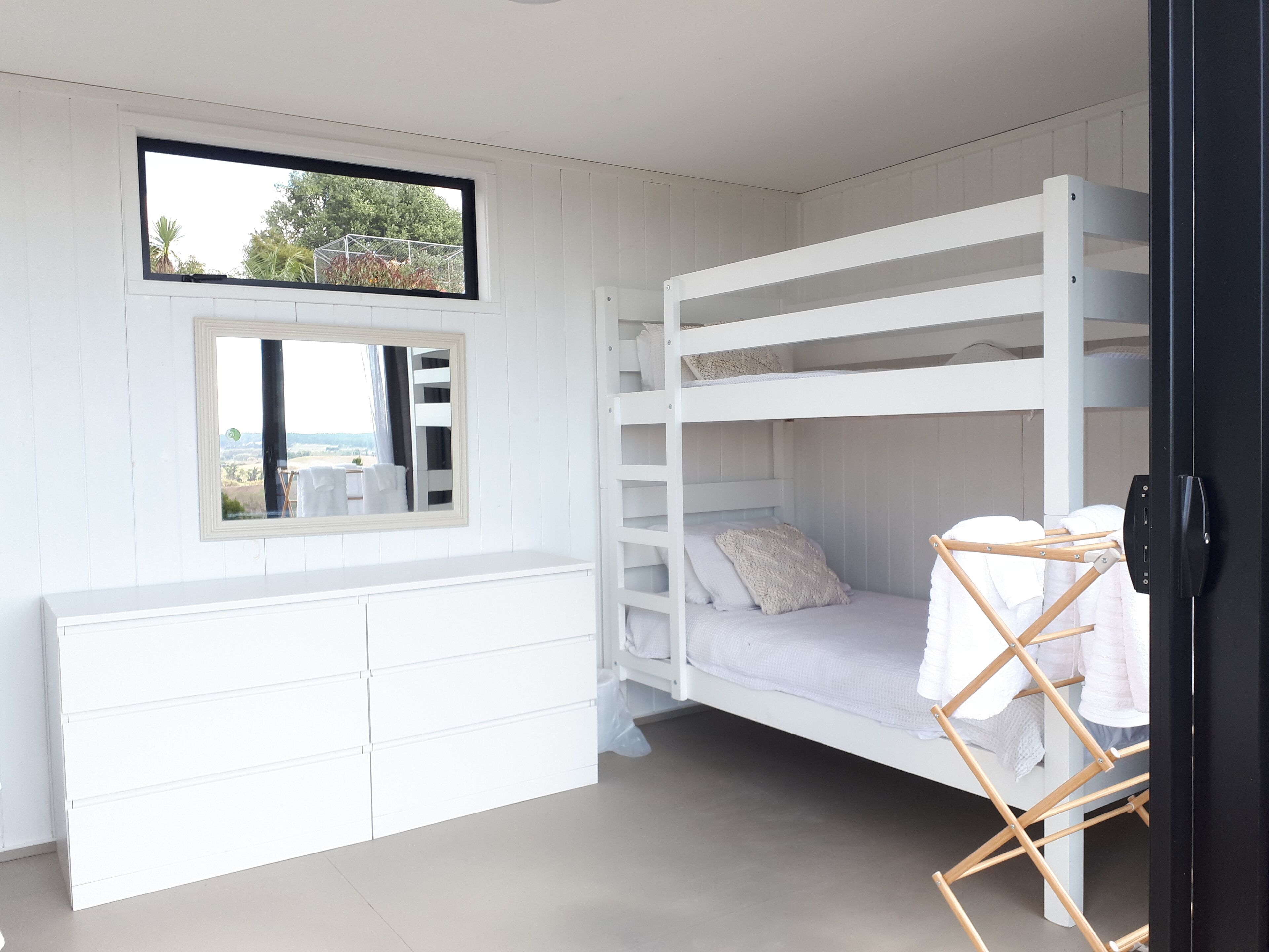 A bunk bed room with a window, a mirror, and a white dresser.