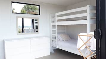 A bunk bed room with a window, a mirror, and a white dresser.