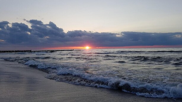 A beach with waves, a sunset, and a pier in the distance. - Kap Ustronie Morskie - 365PAM (Ustronie Morskie)