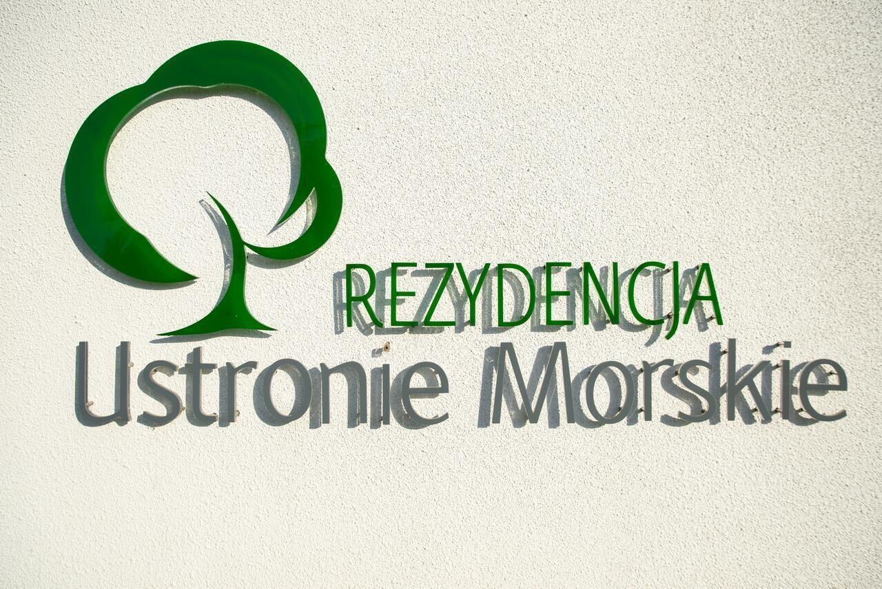 Un logotipo con un árbol estilizado y el texto 'REZYDENCJA Ustronie Morskie'.