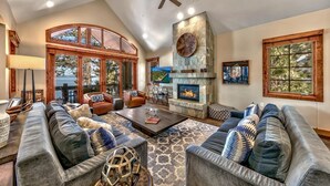 A spacious living room with a fireplace, leather sofas, and a large window overlooking a scenic view. - Exclusive Lakefront Luxury by Heavenly, Hot Tub | PEAK SS14 (South Lake Tahoe)