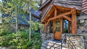 A wooden cabin with a stone foundation, a wooden porch, and a set of stairs leading to the entrance. - Exclusive Lakefront Luxury by Heavenly, Hot Tub | PEAK SS14 (South Lake Tahoe)