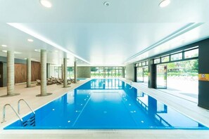 An indoor swimming pool with clear glass walls, a tiled floor, and a ceiling with recessed lighting. - Apartament Polanki Park - 365PAM (Kolobrzeg)