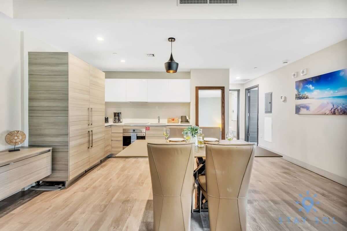 A modern kitchen with white cabinets, a dining area with two chairs, and a painting on the wall.