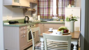 Una cocina con armarios de madera, una mesa de comedor, sillas, un refrigerador y un ventanal con cortinas a cuadros.