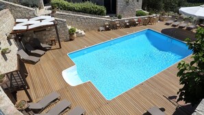 Una piscina rectangular con un muelle de madera alrededor. Hay sillones de descanso y una pequeña mesa cerca de la piscina.