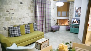 Una sala de estar acogedora con pared de piedra, un sofá verde, una silla de madera, una mesita con un florero y una chimenea.