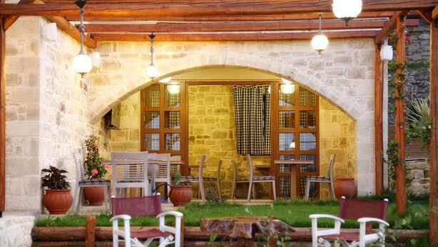 Un patio exterior con paredes de piedra, mobiliario de madera y luces colgantes.