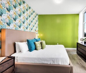 A bedroom with a bed, a dresser, a painting, and a green wall.