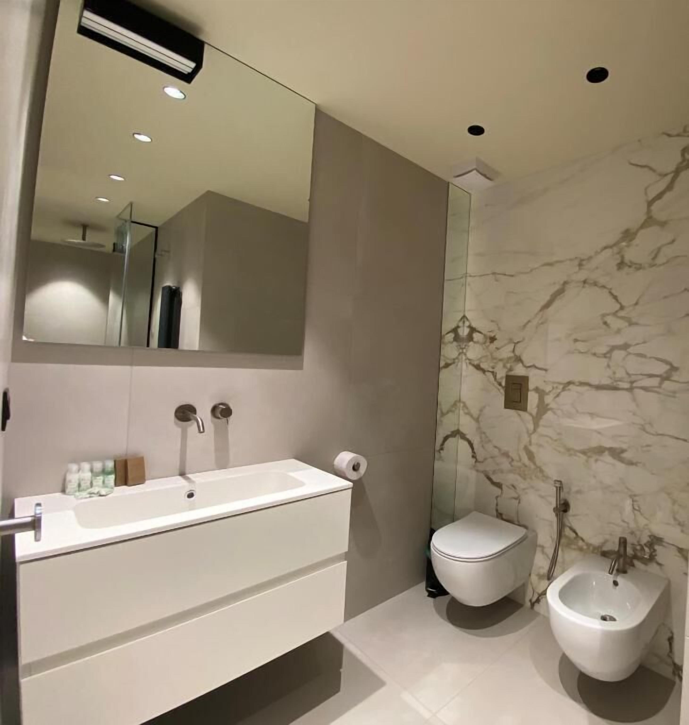 Ein modernes Badezimmer mit einem großen Spiegel, einem weißen Waschbecken, einer Toilette und einem Bidet.