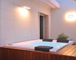 Un jacuzzi con terraza de madera, rodeado de paredes blancas y dos luces empotradas.