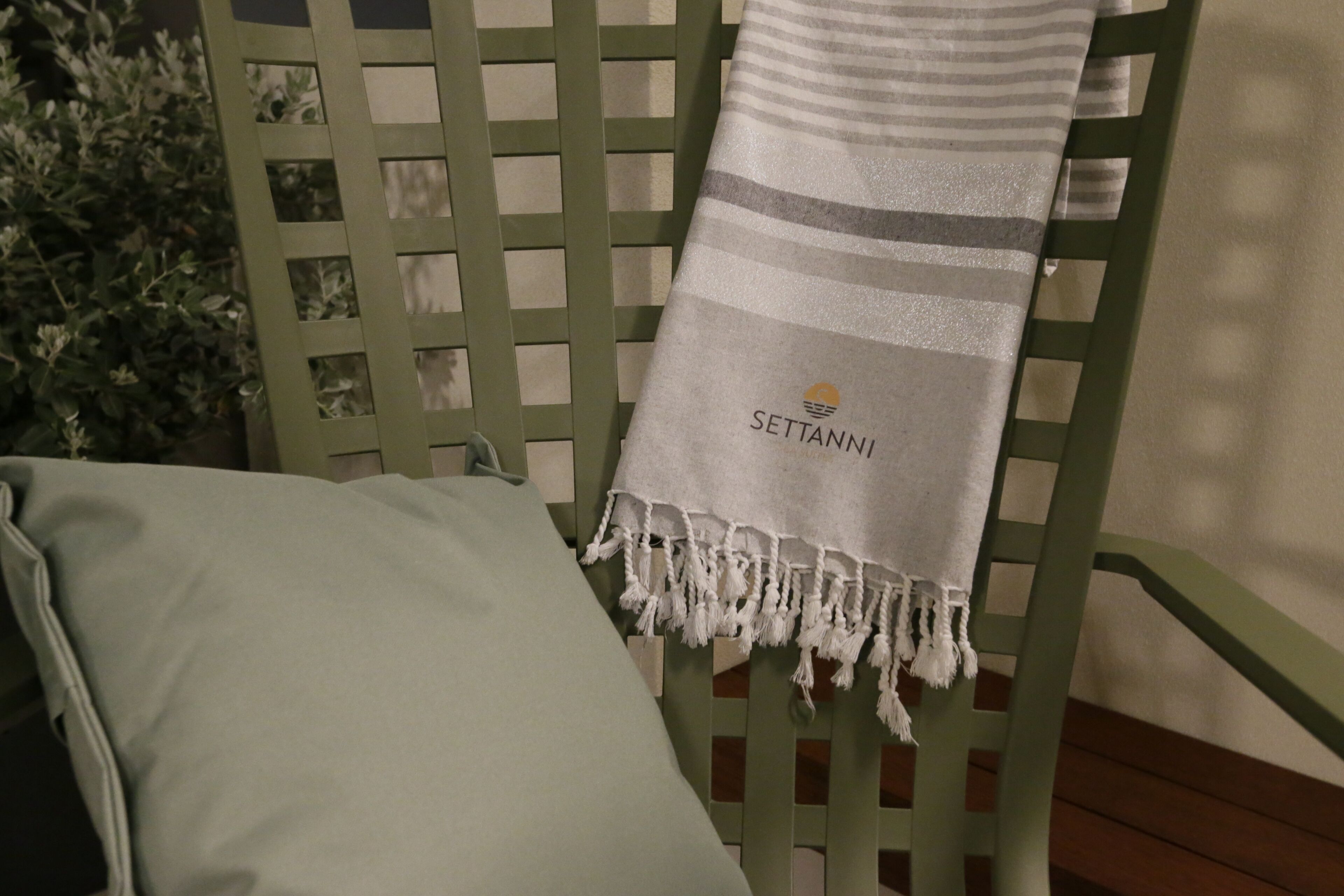 A green chair with a striped towel draped over it, a light green pillow, and a small plant in the background.
