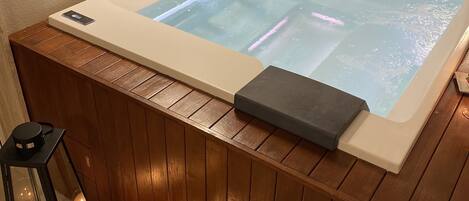 A hot tub with a control panel, wooden paneling, and two lit candles.