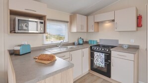 A compact kitchen with a microwave, stove, sink, and cabinets. - Caravan - Sleeps6-pet Friendly-parking Available (Skegness)