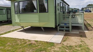A small, single-story, green mobile home with a porch and a small deck. - Caravan - Sleeps6-pet Friendly-parking Available (Skegness)