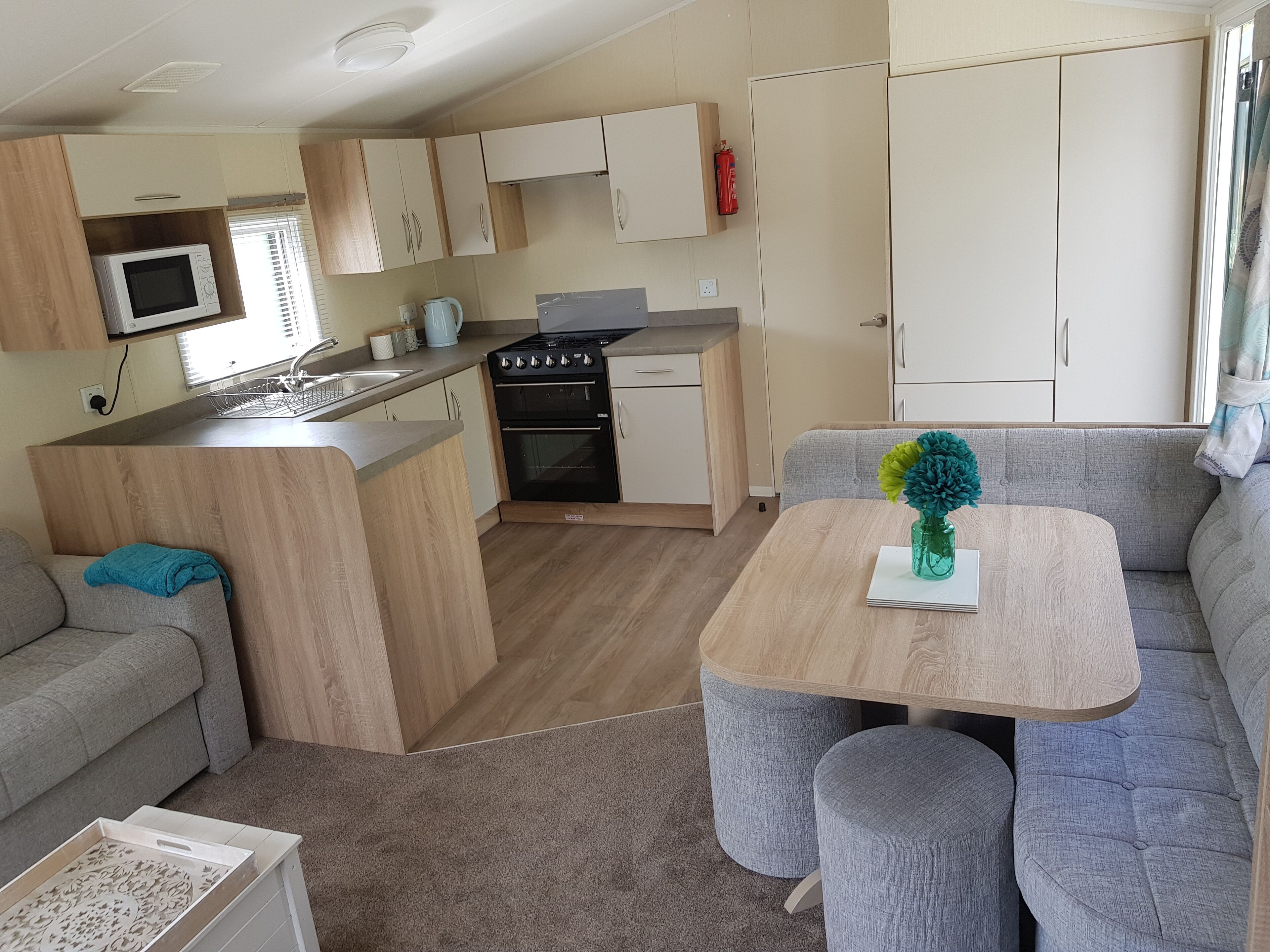 Cocina pequeña con microondas, estufa y lavamanos. Cuenta con una zona de comedor con mesa y dos sillas, además de un sofá.