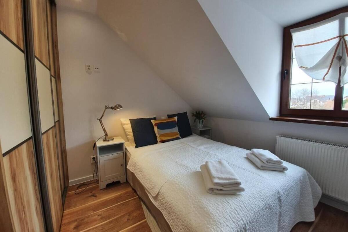A bedroom with a sloped ceiling, a bed with white bedding, a nightstand with a lamp, and a window with a view.