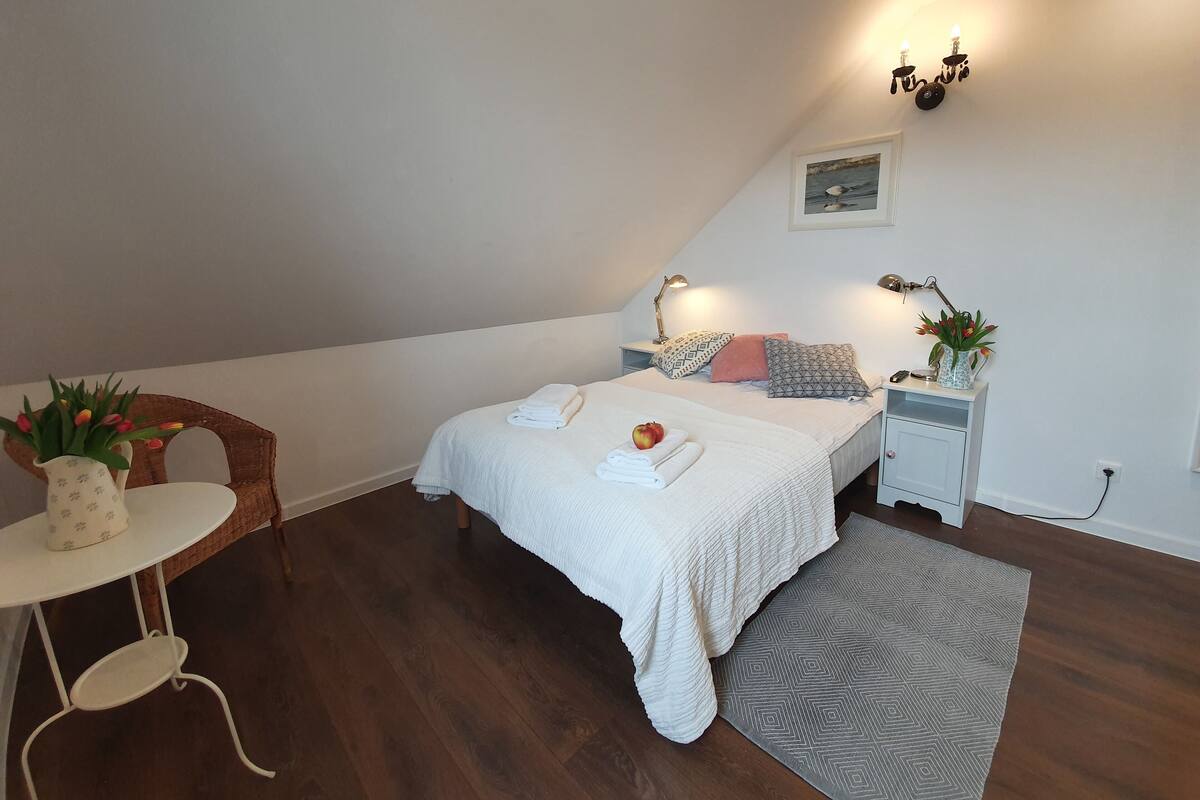 A cozy bedroom with a bed, bedside tables, a small table with a vase of flowers, and a chair.