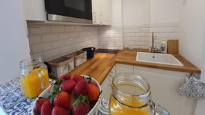 A kitchen with white cabinets, a stainless steel microwave, a sink, and a bowl of strawberries. - Apartamenty Morskie Historie - 365PAM (Kolobrzeg)