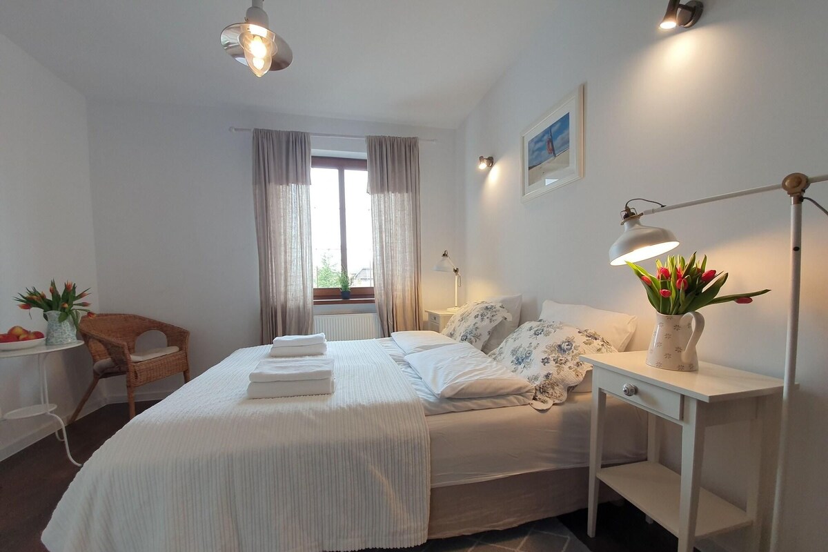 A bedroom with a bed, bedside table, lamp, and a window with curtains.