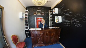 A bar area with a chalkboard menu listing special beers and prices, a red telephone booth, and a counter with a woman behind it.