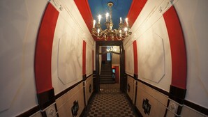 A hallway with a checkered floor, red and white walls, and a chandelier.