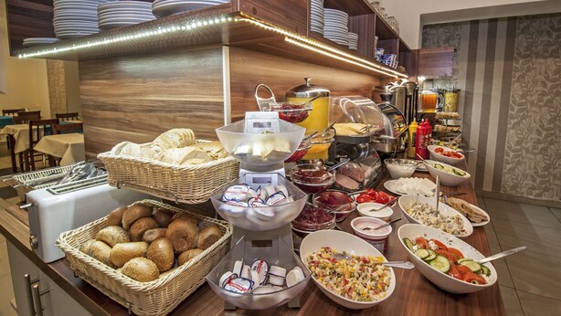 A buffet with various food items, including bread, cheese, and salads, in a well-lit room with wooden decor and a counter.
