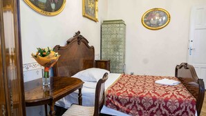 A bedroom with a wooden bed, a bedside table with a vase of flowers, a chair, and a wooden desk.