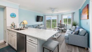A modern kitchen with a large island, a dining area with a table and chairs, a sofa, and a TV mounted on the wall. - Snorkel & Dive Legendary Coral Reefs - Then Relax Poolside with a Drink! (Tavernier)
