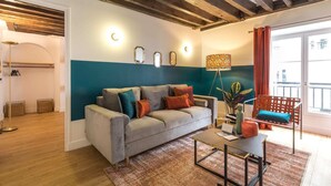 Un salón moderno con un sofá gris, vigas de madera en el techo y vistas al exterior.