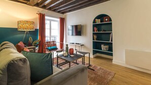 Una sala de estar con sofá, mesa de centro, televisor, estantería y ventana con cortinas.