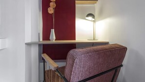 Una silla con asiento y respaldo trenzados, un jarrón blanco con flores secas y una lámpara de pie sobre una estantería de madera.