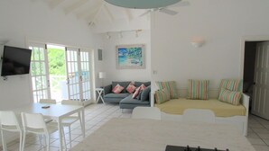 A spacious living area with a dining table, white chairs, a sofa with colorful cushions, and a television mounted on the wall. - Jolly Harbour, 3 bedroom villa, pool, close to beach and all amenities. (Jolly Harbour)