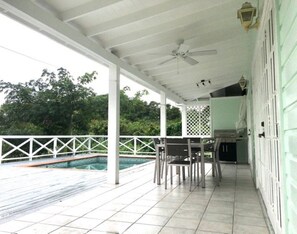 A covered outdoor area with a pool, a table and chairs, and a ceiling fan.