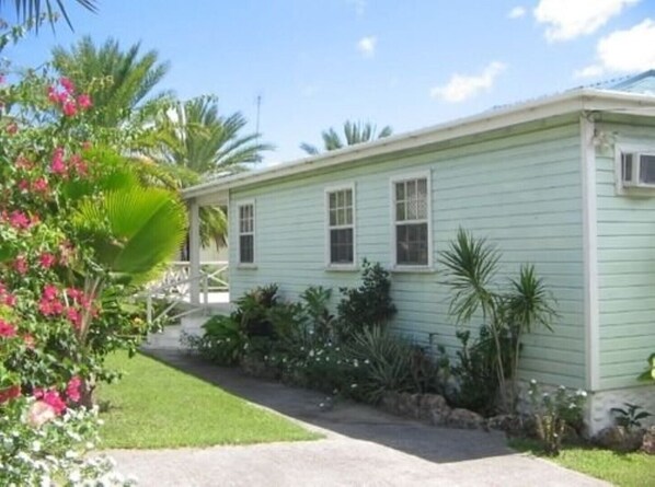 A single-story house with a light green exterior, a front porch, and a well-maintained garden with various plants and flowers.