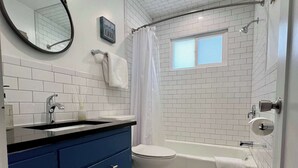 Un baño con paredes de azulejos blancos, un tocador azul, un inodoro, una bañera y una cortina de ducha.