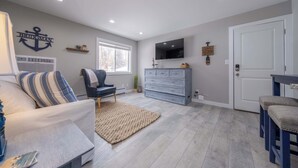 Una sala de estar con sofá, una silla, televisor, cómoda y puerta.