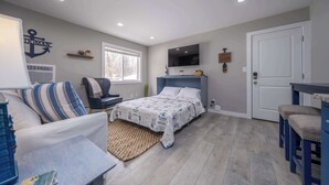 Un dormitorio con cama, una silla, televisor y puerta.