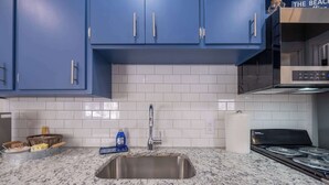 Una cocina con armarios azules, un lavamanos de acero inoxidable, una estufa a gas y salpicadero de azulejos blancos.