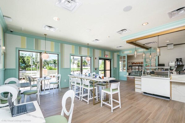 A spacious indoor area with a long table and chairs, a counter with a display case, and a view through large windows. - 1570 Carey Palm Circle (Kissimmee)