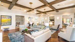 A spacious living room with a high ceiling, wooden beams, and modern lighting fixtures.