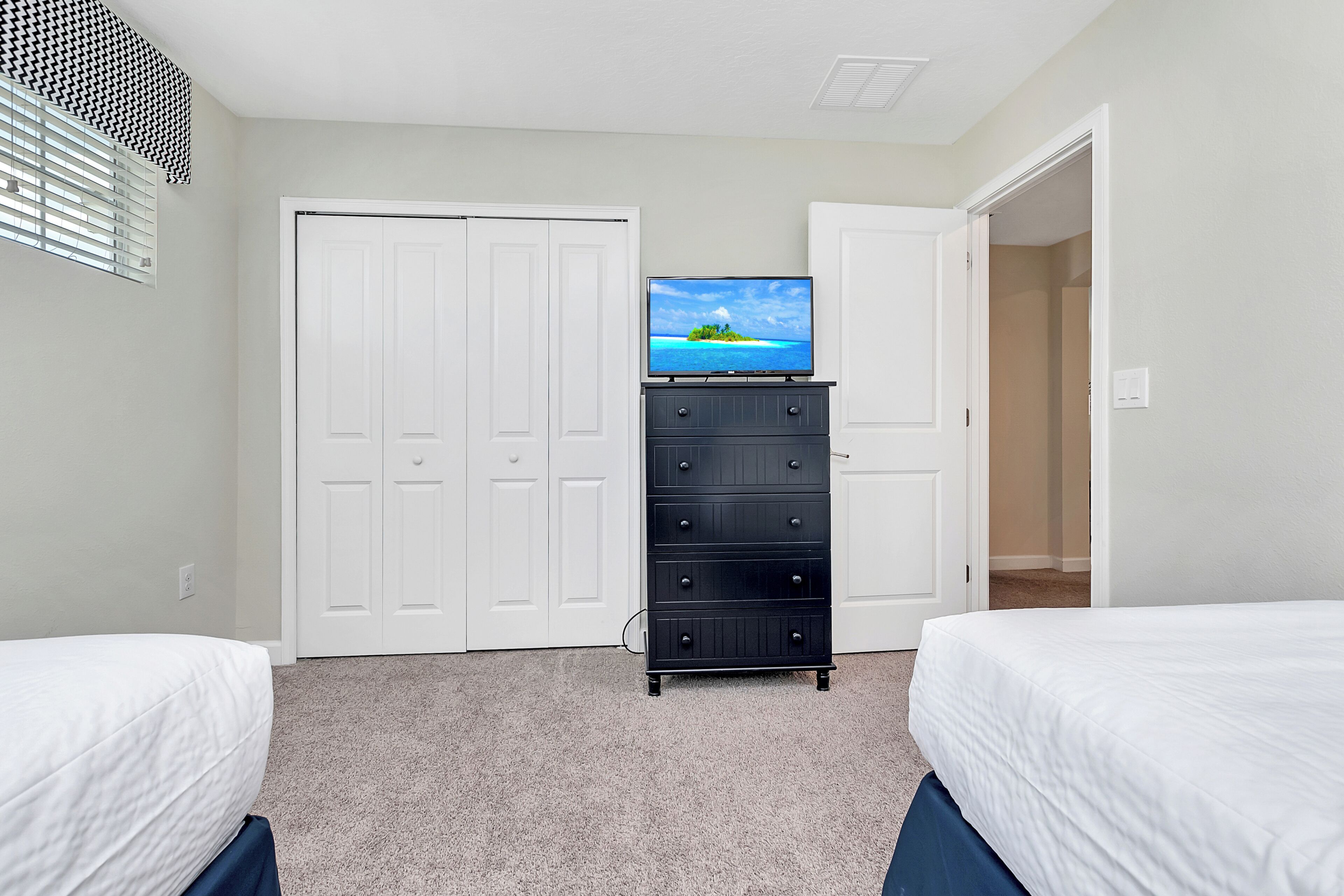 A bedroom with two beds, a dresser, a TV on top of the dresser, and a closet.