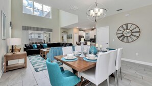 A spacious dining area with a wooden table set for four, white chairs, and a large wall clock.